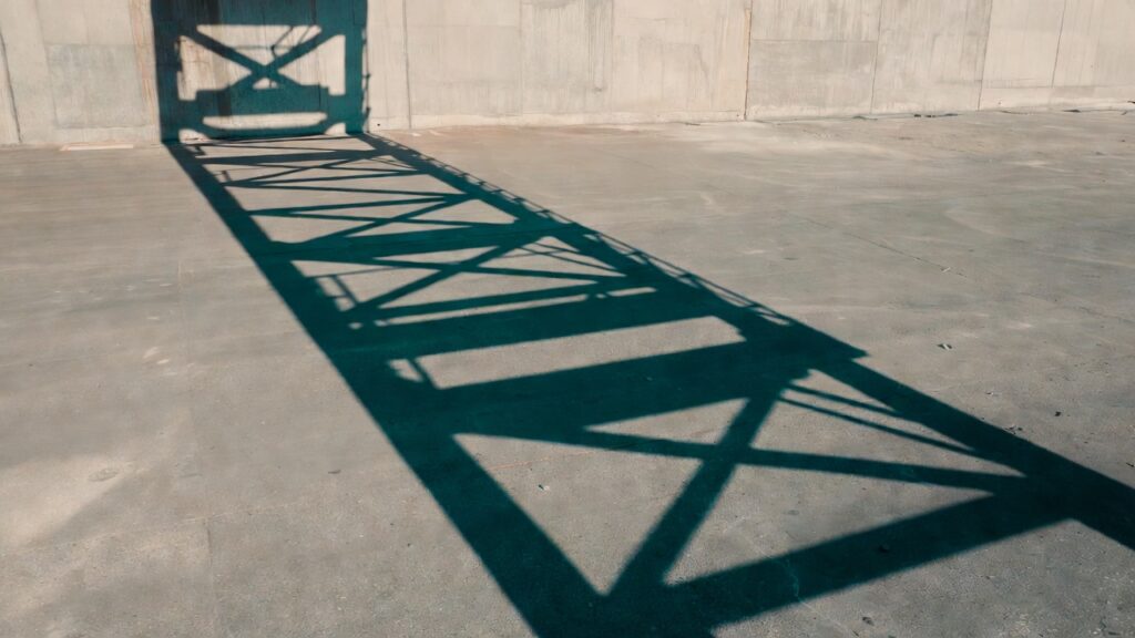 Sombra geométrica de estructura de andamio proyectada sobre piso de concreto industrial, imagen conceptual sobre seguridad en altura en Chile